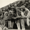 Six black women (Howard University students) in audience, sitting in stadium watching game, men shown sitting behind them. All but one of the women wear cloche hats. The woman on the extreme right was identified as Elise Dowling.
